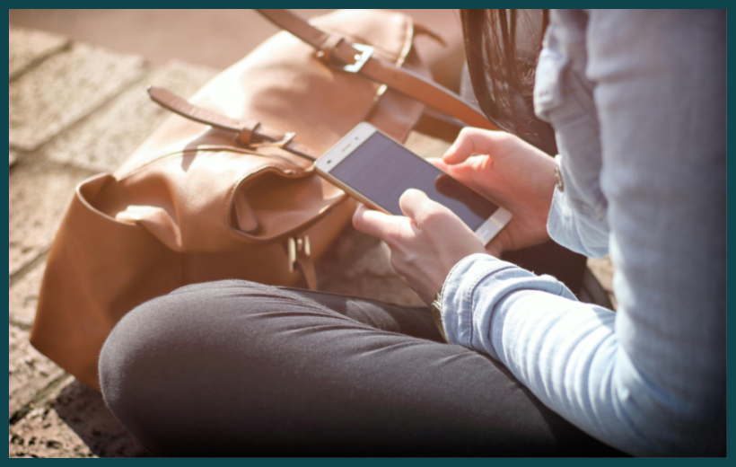 Image of woman holding her smartphone in her lap with a brown leather bag in front of her by Tofros.com via Pexels.